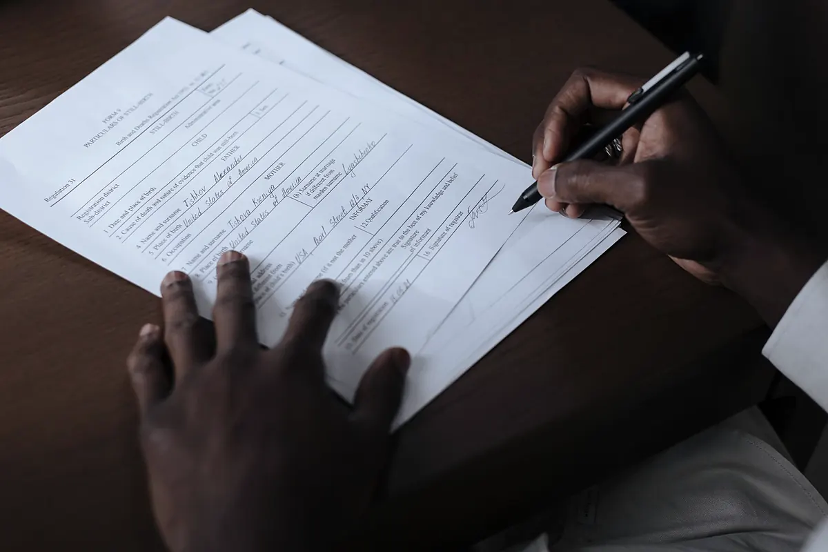 Mãos assinando documento sobre mesa de madeira escura